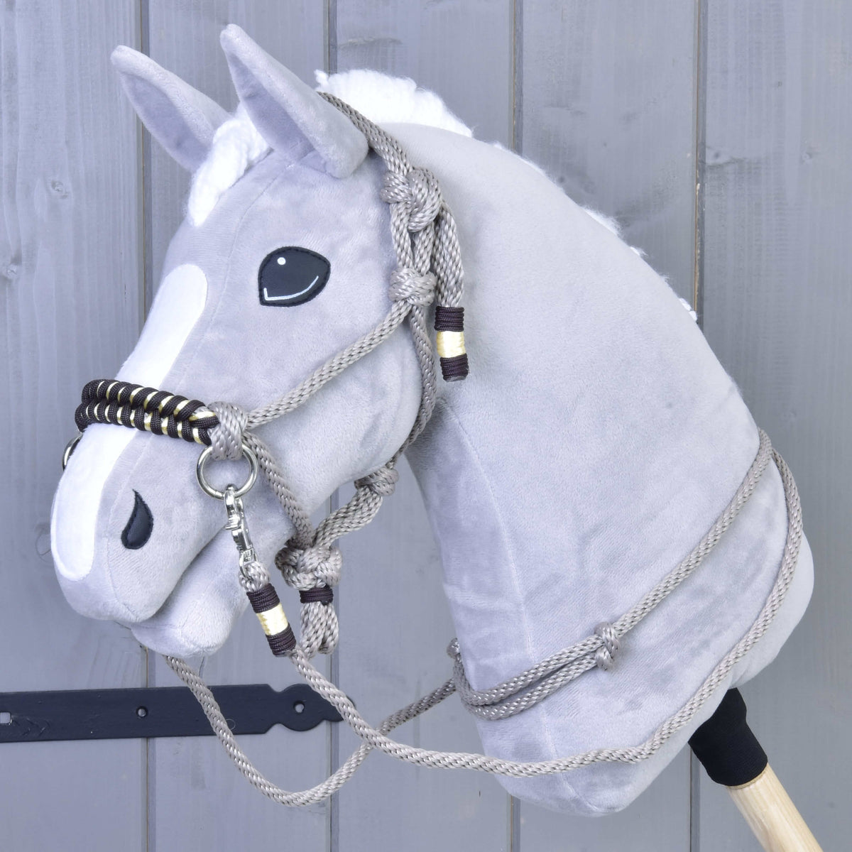 The Rope set Splendid by Hobby Horse LarDen features a gray plush hobby horse with a white mane, black eyes, and rope bridle and reins, shown against a gray wooden wall.