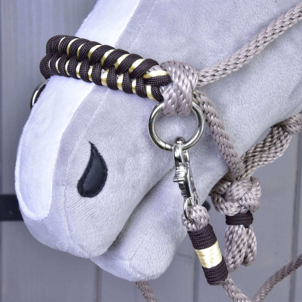 A close-up of a gray Hobby Horse LarDen with the Rope set Splendid—a braided halter with gold and black accents, reins, and a metal clasp attached to a nose ring.