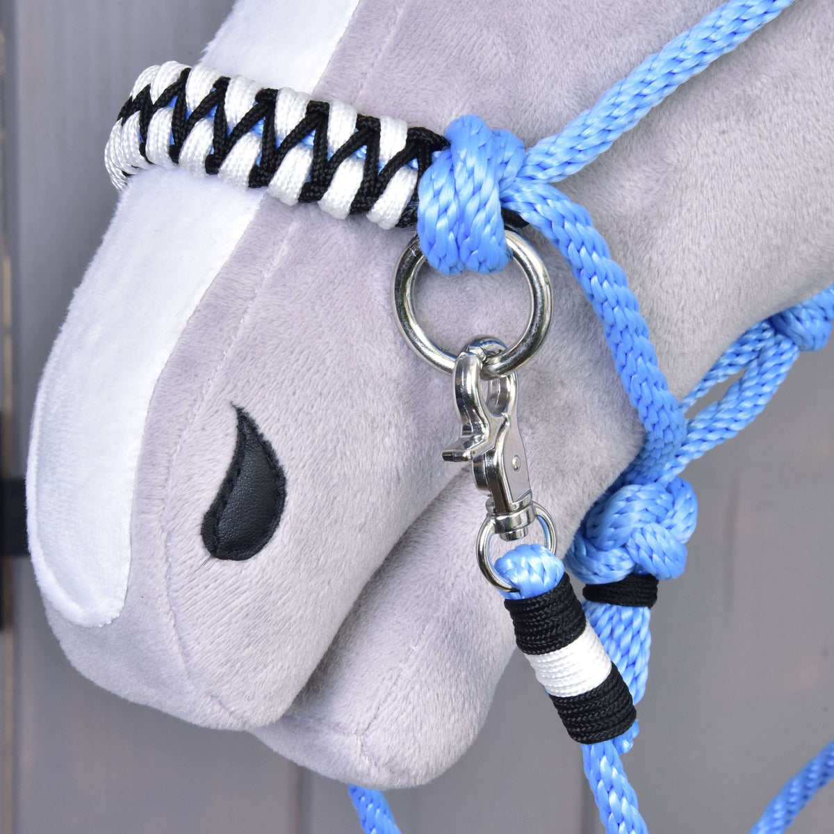 Close-up of a Hobby Horse's plush head with a white blaze, wearing the Rope set Malibu blue halter with black and white accents, plus reins attached to a silver clip and metal ring.
