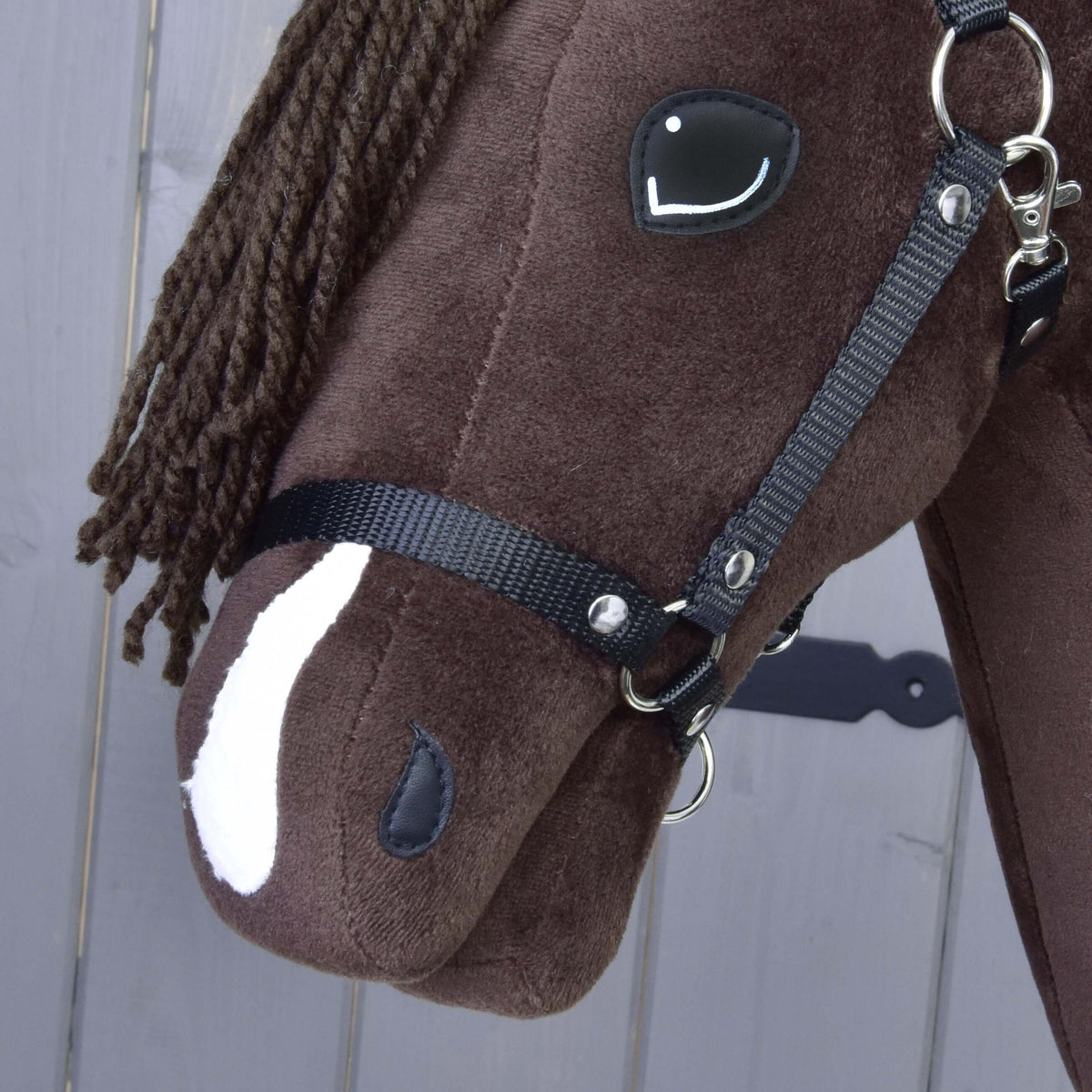 Close-up of the Hobby Horse LarDen's Hobby Horse Chianti with Black Halter, inspired by the American Quarter Horse, featuring a black yarn mane, white nose patch, and black bridle against a gray wooden background.