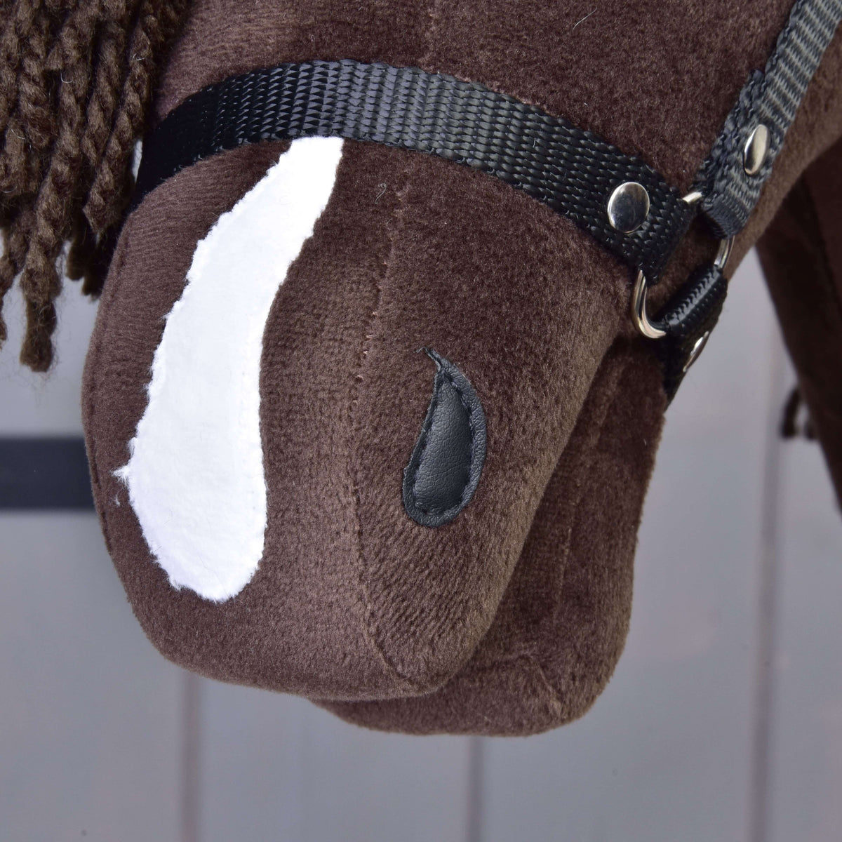 Close-up of the Hobby Horse LarDen "Hobby Horse Chianti with Black Halter": a brown fabric toy horse's head with a white patch, black halter, button eye, and brown yarn mane against a softly lined light background.