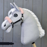 A Hobby Horse LarDen plush hobby horse with a grey face, white mane, and a black halter with old rose fur in leatherette, shown on a wooden background.