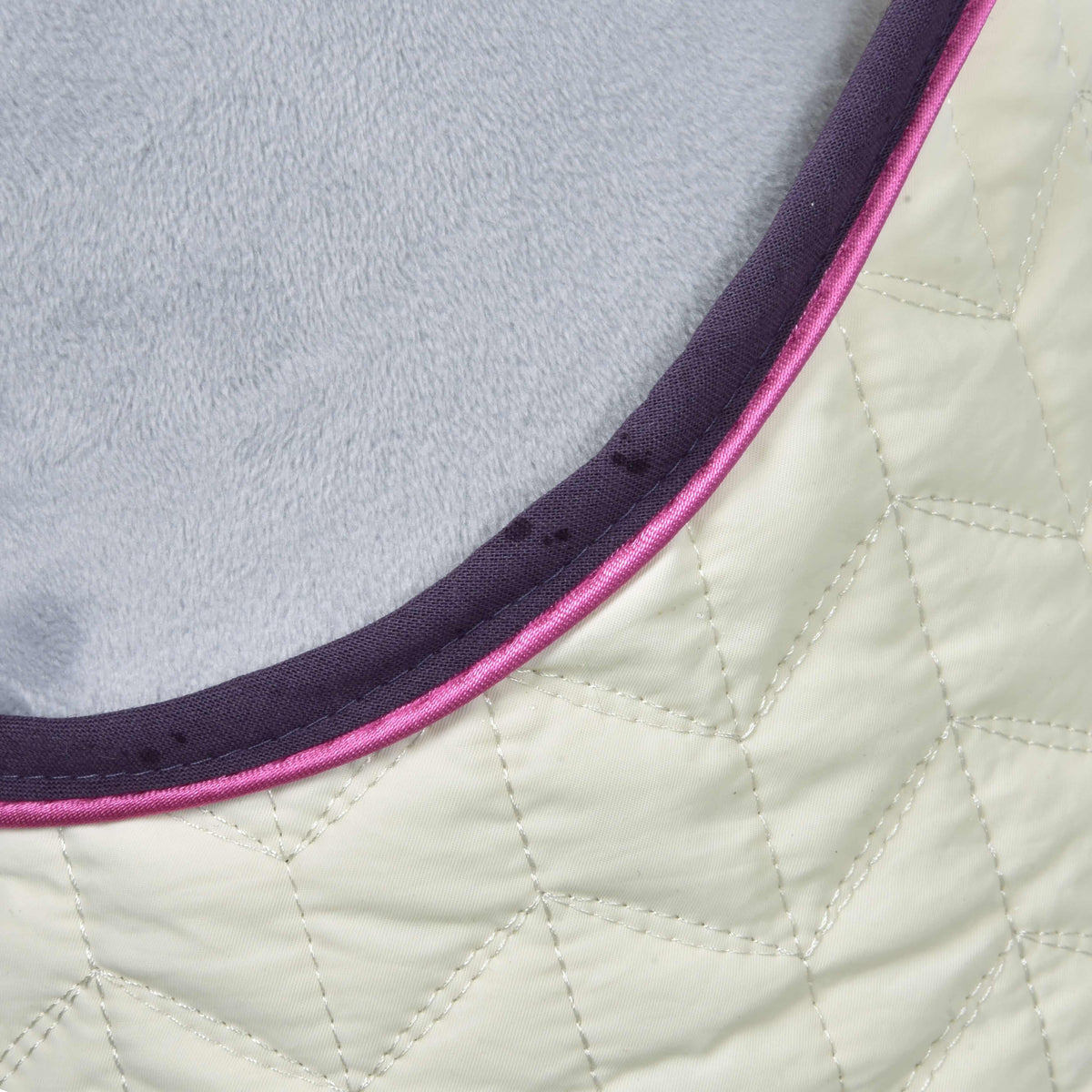 Close-up of Set Supreme Crema by Hobby Horse LarDen: quilted fabric with a geometric stitched pattern, bordered with dark purple and pink trim, and lined with soft light gray material.