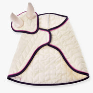 The Set Supreme Crema by Hobby Horse LarDen is a quilted, cream garment with purple trim and pink accents, designed to wrap cozily around the body and featuring horn-like ear bonnets. Shown laid flat on a white background.