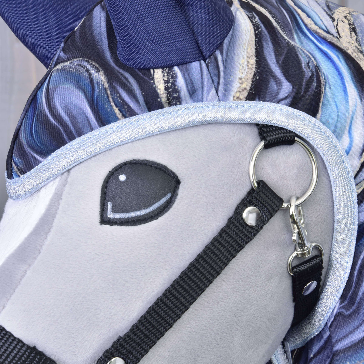 Close-up of the plush head of Hobby Horse LarDen's Raincoat Galaxy Cobalt, showing a soft gray face, embroidered black eye, shiny silver bridle trim, and a blue-and-white patterned mane—great for matching your favorite hobby horse accessories.