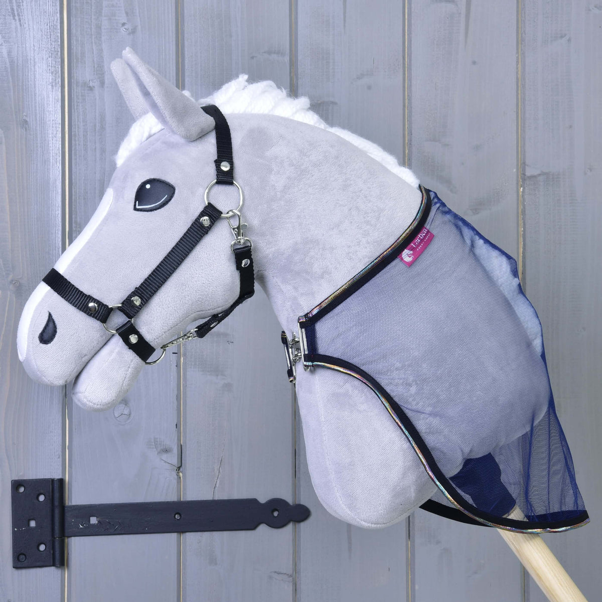 A plush gray Hobby Horse LarDen with a black bridle and the Fly sheet LarDen attached, shown against a light gray wooden door with a black hinge.