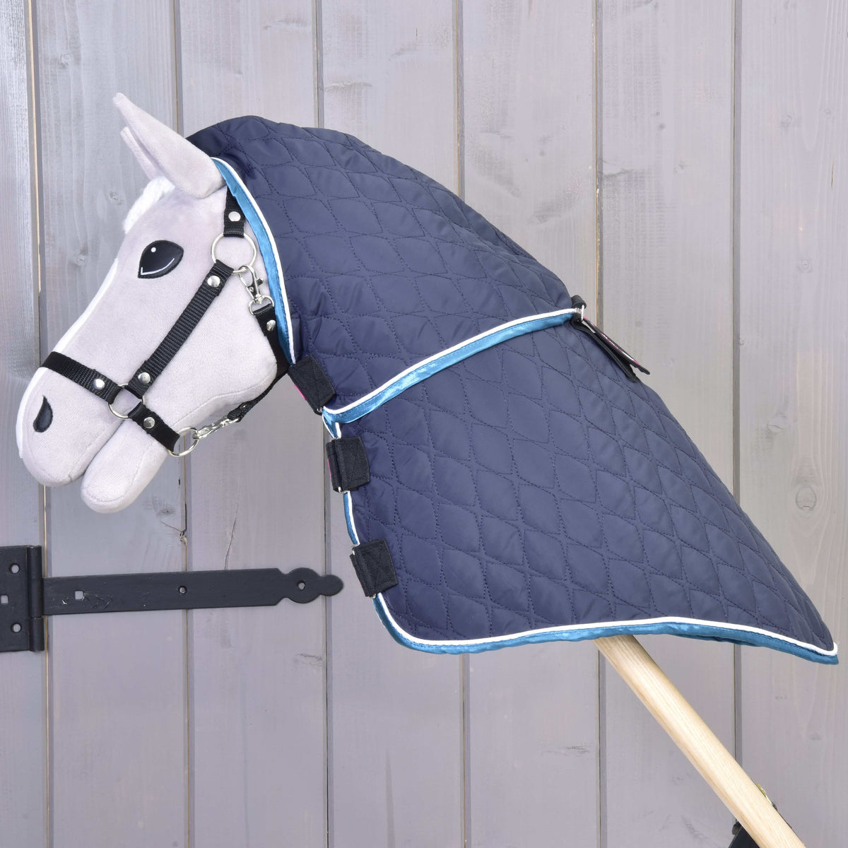 Grey Hobby Horse in a black halter wearing the navy quilted blanket with the neck cover attached, blue and white trim