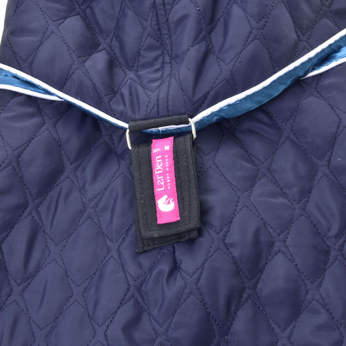 Close-up of the pink LarDen label on the strap joining the neck cover to the navy quilted Hobby Horse blanket