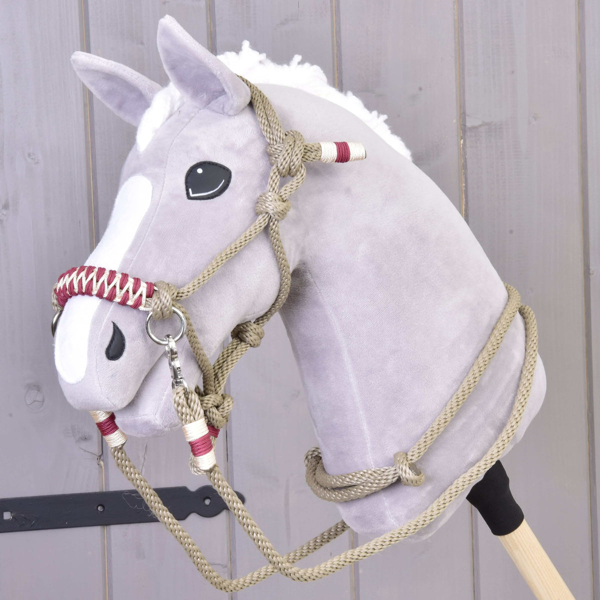 A gray plush hobby horse with a white mane and blaze, wearing the Rope set Eleganza by Hobby Horse LarDen, stands in front of a light wooden wall.