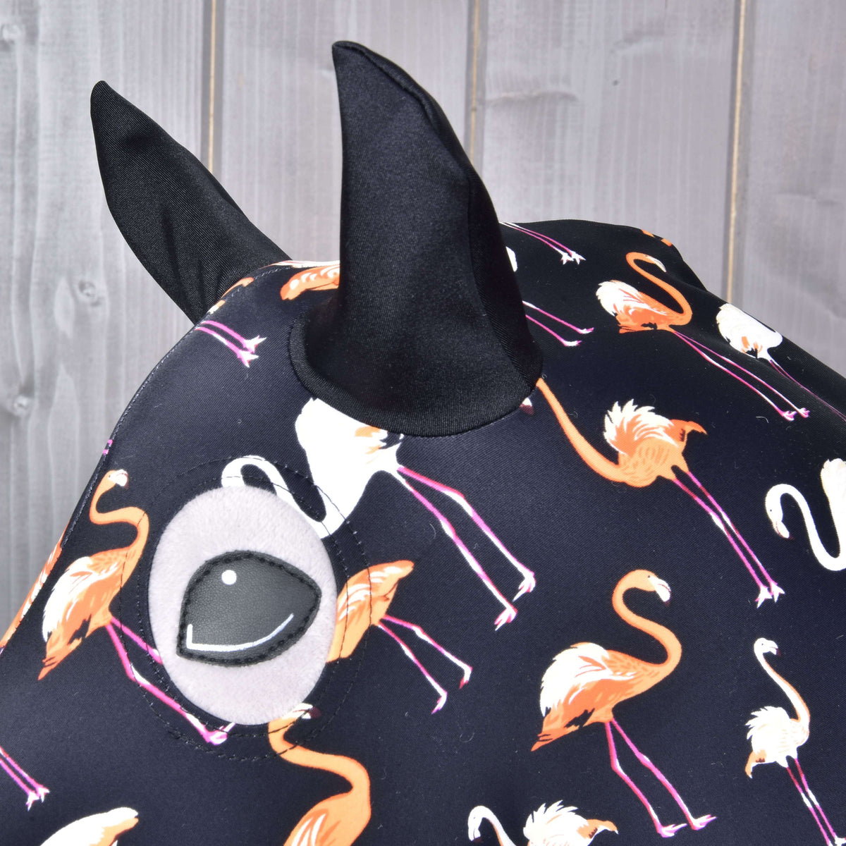 Close-up of the black ears and eye opening on the flamingo print Lycra suit on a grey Hobby Horse