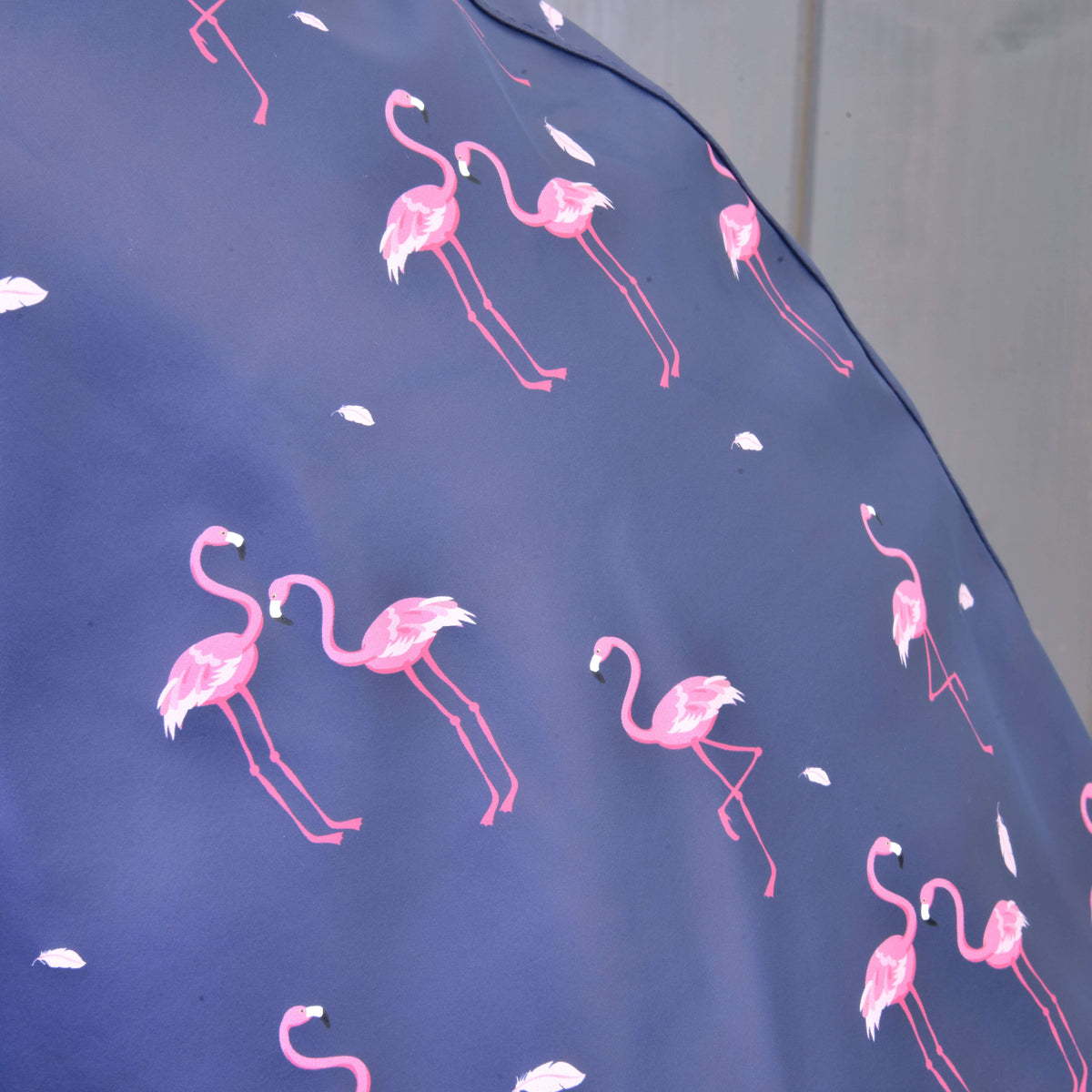 A close-up of Raincoat Flamingo by Hobby Horse LarDen shows blue fabric with pink flamingos and white feathers, featuring a soft, out-of-focus background—perfect for all-weather adventures or playful days.