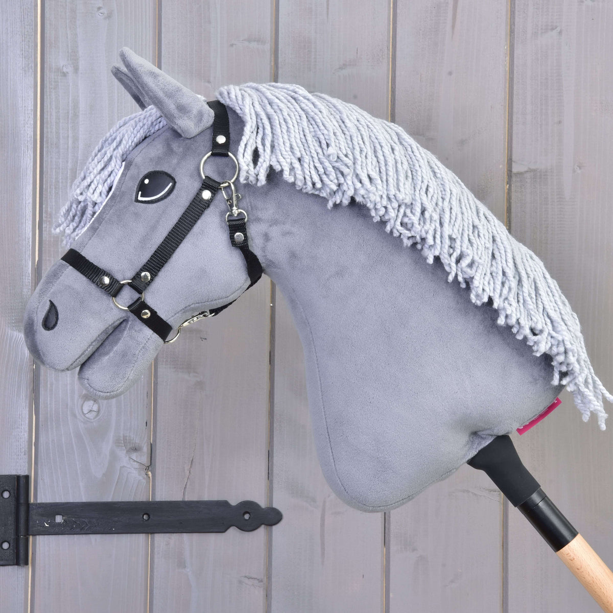 The Hobby Horse Grace with Black Halter by Hobby Horse LarDen is a gray Dutch Warmblood with a yarn mane, mounted on a wooden stick and shown against a wooden panel wall.