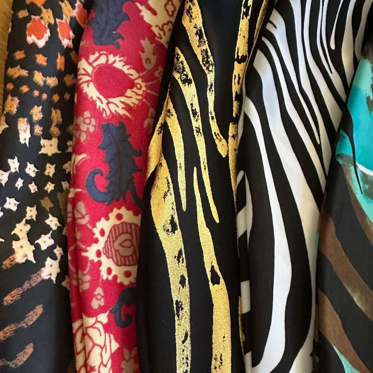 A close-up of five colorful fabrics—perfect for Hobby Horse accessories—with animal print, red and cream floral, gold and black animal stripes, black and white zebra stripes, and turquoise with brown swirls.