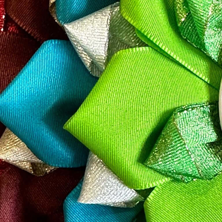 Close-up of colorful, layered ribbon bows in green, blue, silver, and maroon, perfect for decorating a Hobby Horse or adding flair to your next Hobby Horsing accessory with their shiny and textured fabric.