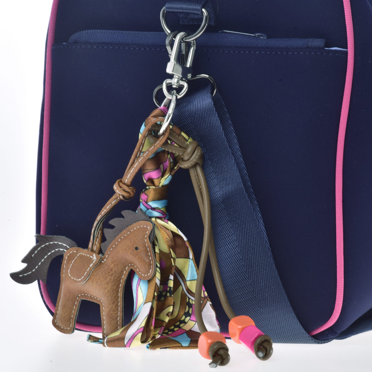 Keychain Horse Brown hanging from a navy bag with pink piping, its brown cords and colourful scarf wrapped around the clip