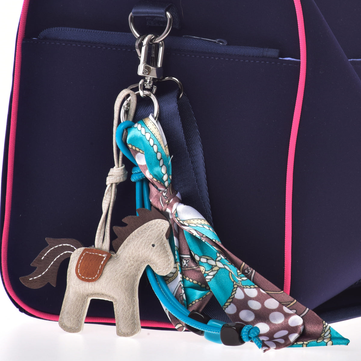 Keychain Horse Grey clipped to the strap ring of a navy bag with pink piping, with turquoise beads and a tied scarf
