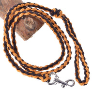 The Hobby Horse LarDen Knitted Lead Rope Pomello, featuring orange and black strands and a premium carabiner clasp, is coiled on a wooden log for secure and stylish attachment.