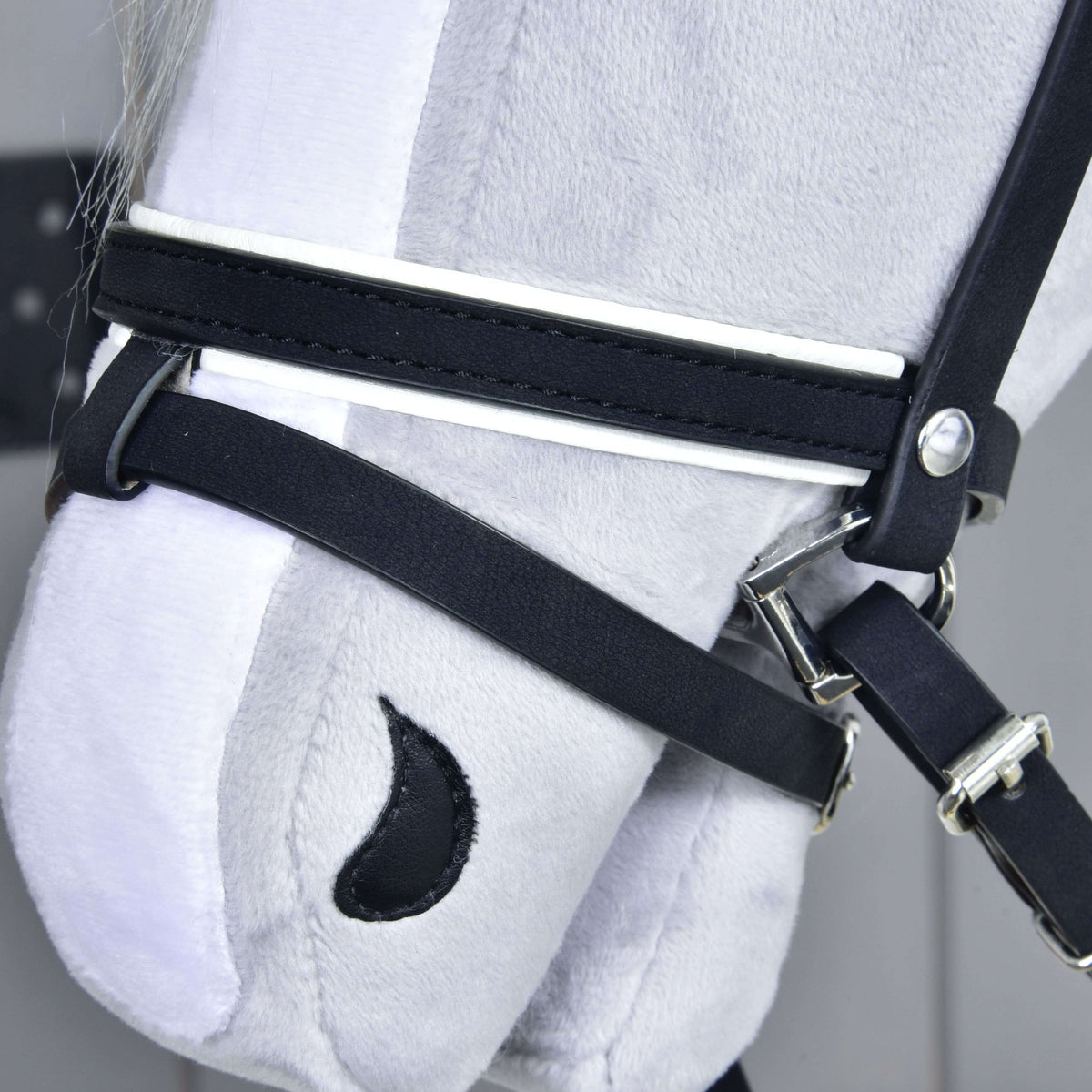 Close-up of a gray plush horse's head from Hobby Horse LarDen, wearing the Complete De Luxe bridle with 2 browbands. Embroidered features like a black crescent nostril stand out against a light background.