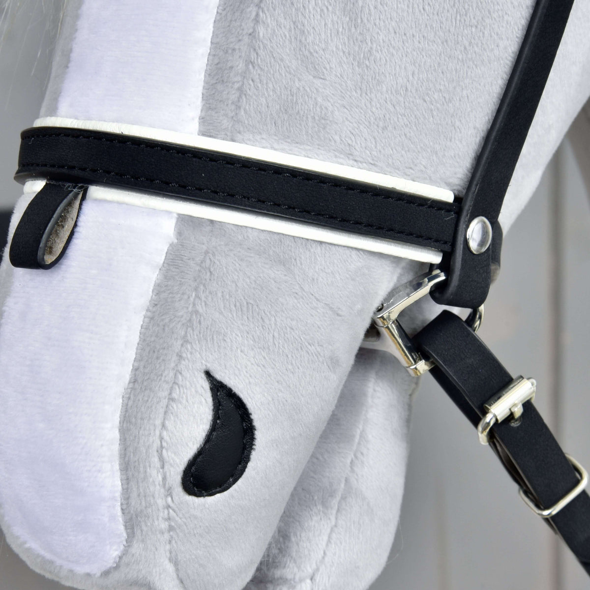 Close-up of a gray plush Hobby Horse LarDen toy’s head, showcasing the Complete De Luxe bridle with 2 detachable browbands, combined noseband, metal buckles, and a stitched black eye on soft fabric.