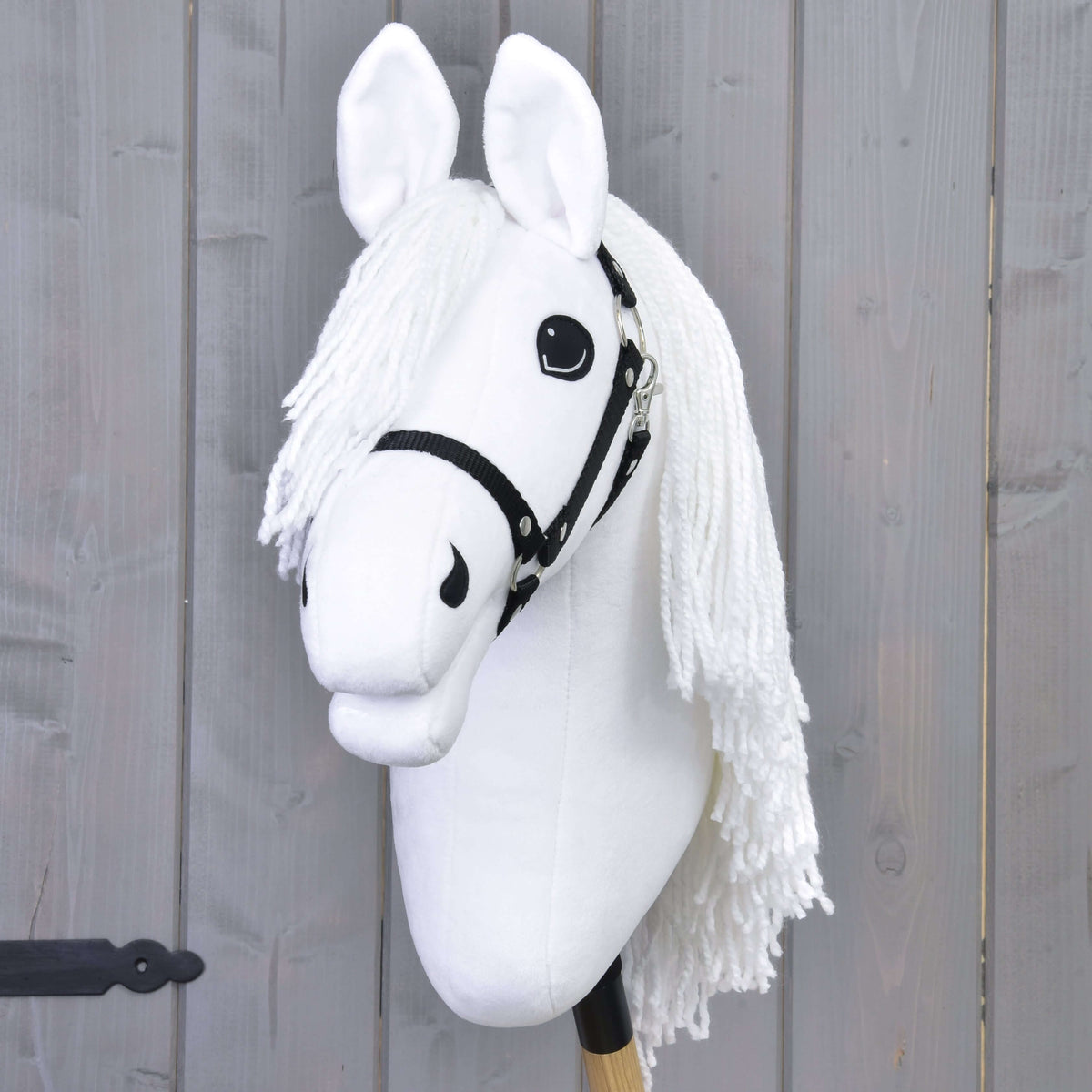 The Hobby Horse Lady with Black Halter by Hobby Horse LarDen features a white mane and expressive eyes on a wooden stick against a gray plank background—ideal for imaginative dressage play inspired by Lipizzaner horses.