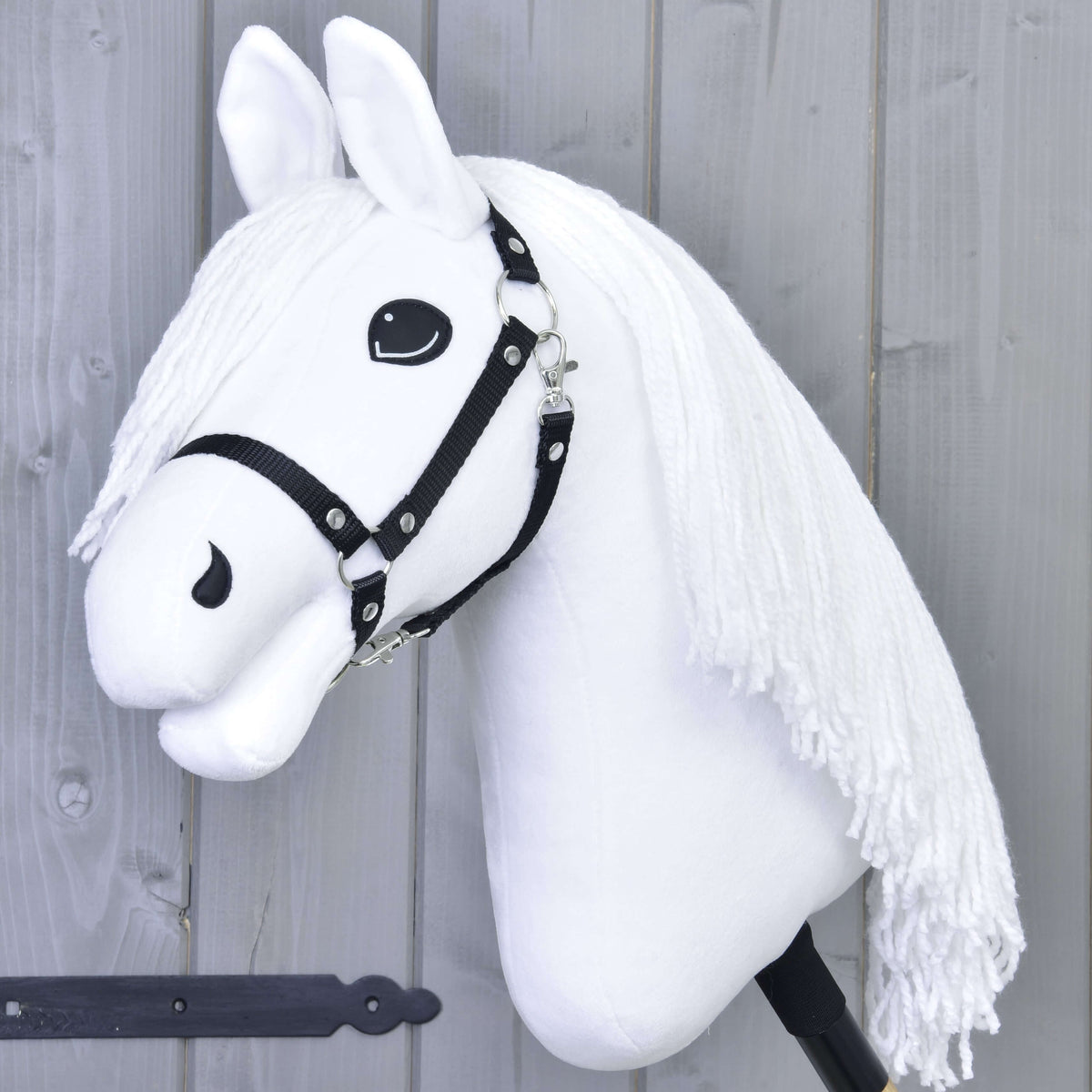 The Hobby Horse LarDen "Hobby Horse Lady with Black Halter" features a white horse with a black halter and long yarn mane on a stick, posed as if ready for dressage in front of a light gray wooden wall.