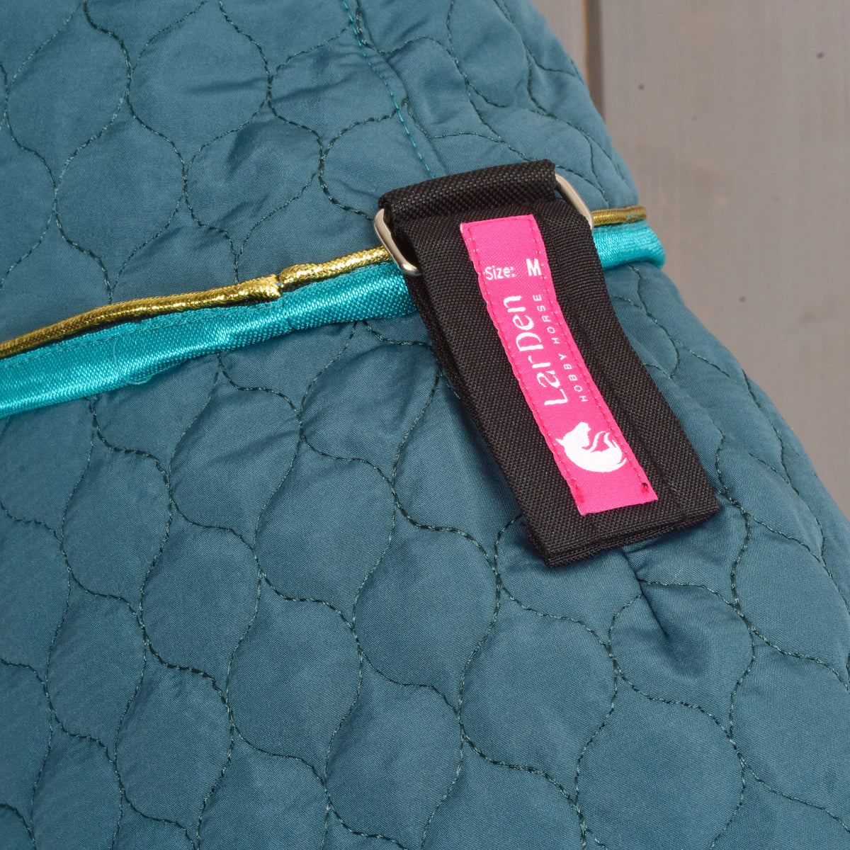 Close-up of the green quilted Hobby Horse blanket with turquoise trim and LarDen fastening label