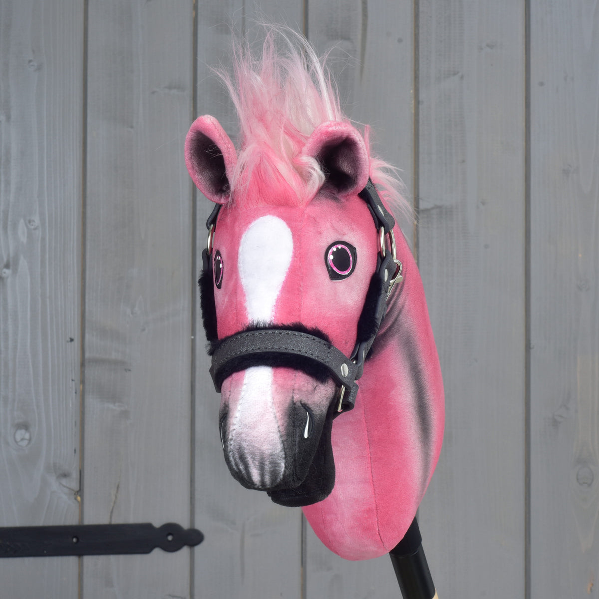 A limited edition Hobby Horse LarDen Pinkie with a glittery halter, featuring pink and white plush fur and a fluffy pink mane, is positioned against a gray wooden background.