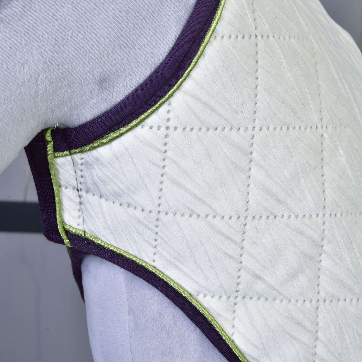 Close-up of quilted, padded white fabric with purple and green trim in a diamond pattern, covering a curved surface—part of the Set Leonardo by Hobby Horse LarDen.
