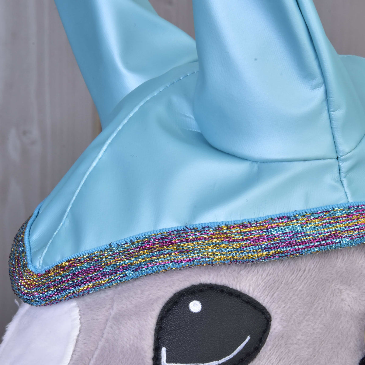 Close-up of a Hobby Horse LarDen Raincoat Light Blue, featuring shiny blue details, sparkly multicolored trim, and soft gray fabric—perfect for your all-weather Hobby Horse adventures.