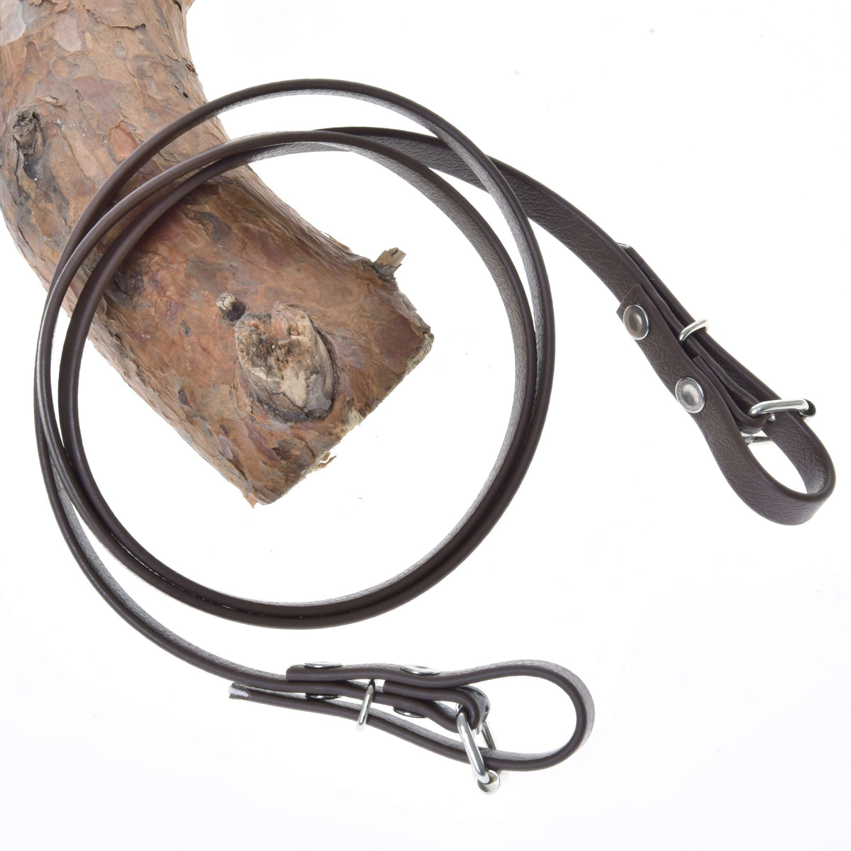 The Hobby Horse LarDen "Reins Light brown" are draped around a textured tree branch on a white background, highlighting their stylish leather look and metal hardware reminiscent of bitless bridle reins.