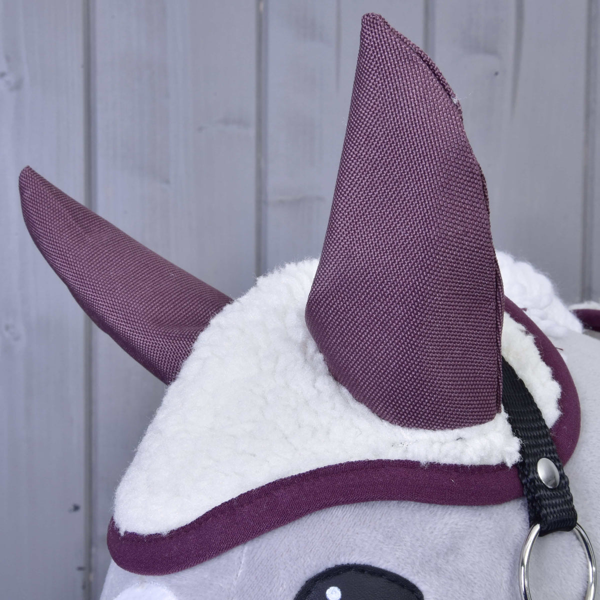 Close-up of the Set Loret plush animal head by Hobby Horse LarDen, showing white fluffy fabric, large purple bonnet-style ears, and a black strap on a light gray wooden background.