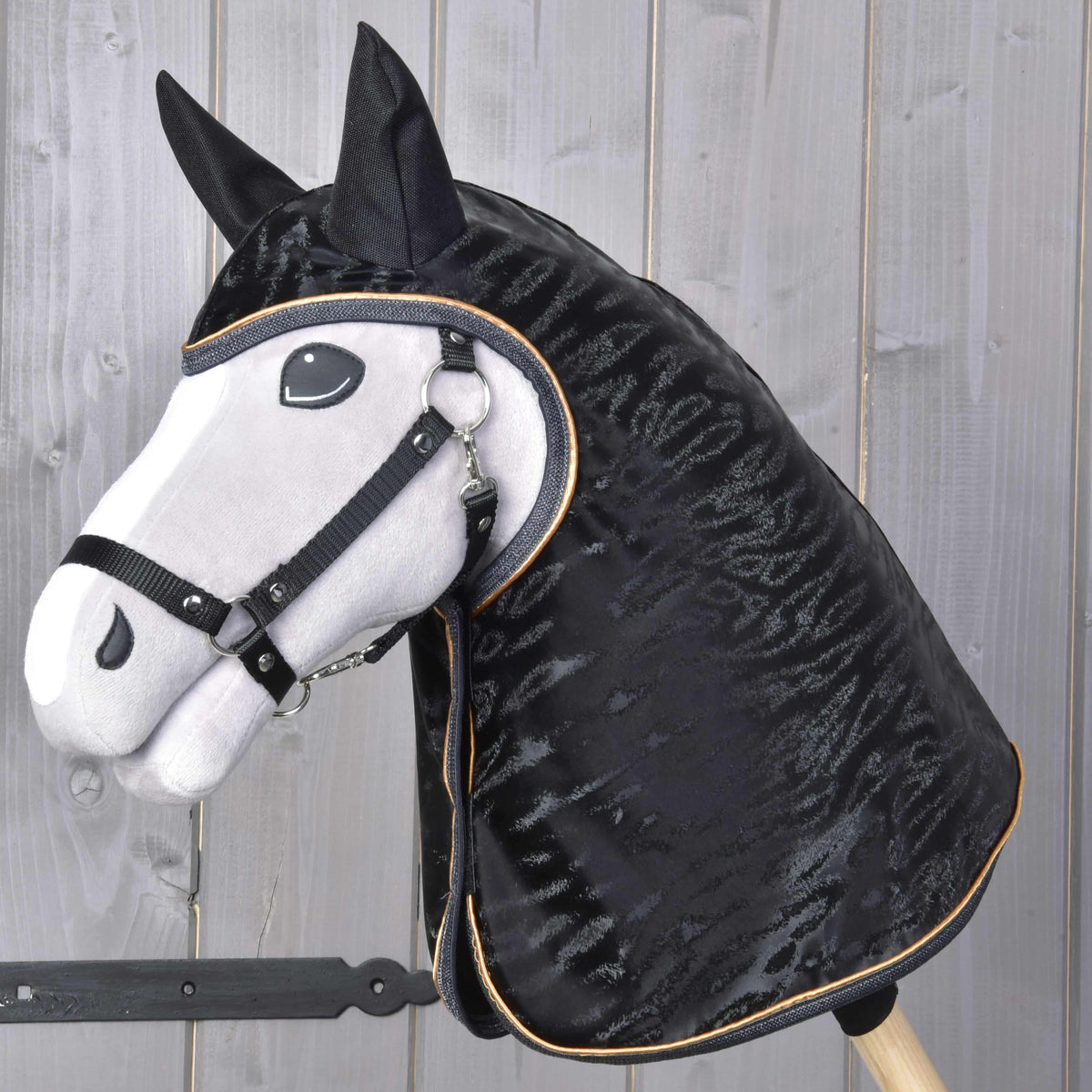 Grey Hobby Horse in a black halter wearing the glossy black raincoat with ear covers and gold piping over its head and neck