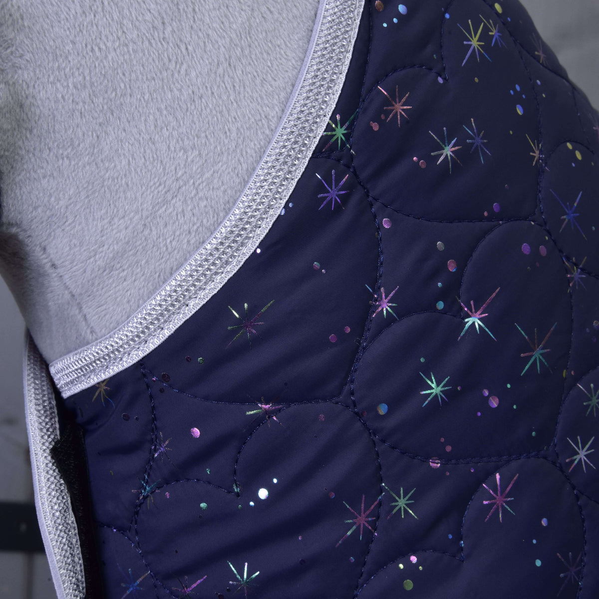 Close-up of a quilted, dark blue Set Magic blanket by Hobby Horse LarDen, featuring iridescent stars and silver trim, worn by a light-colored horse. Combines style with insect protection for greater comfort.