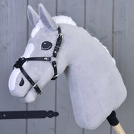 The Hobby Horse LarDen Noseband Mexico Black Padded is a gray plush hobby horse with a white mane, black bridle, and leatherette noseband on a wooden stick, set against a gray wooden paneled background.