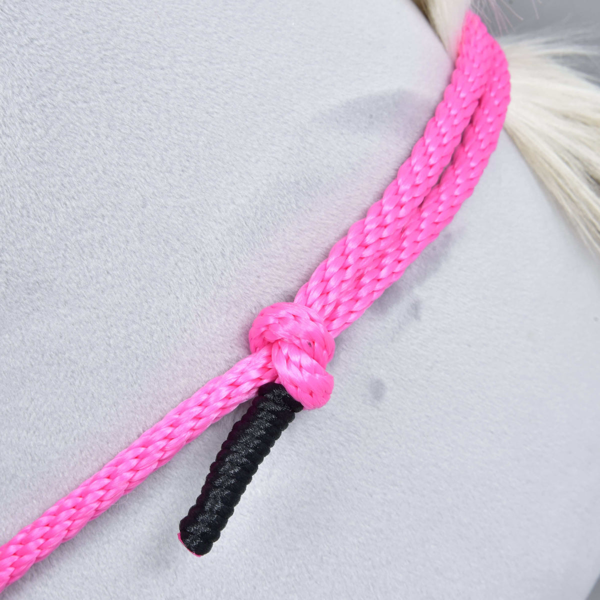 Close-up of Cordeo Pink Festive by Hobby Horse LarDen—a vibrant pink handmade cordeo rope with a black-ended strand, tied in a knot around a pale gray surface. Perfect for bridleless riding; background is smooth with faint marks.
