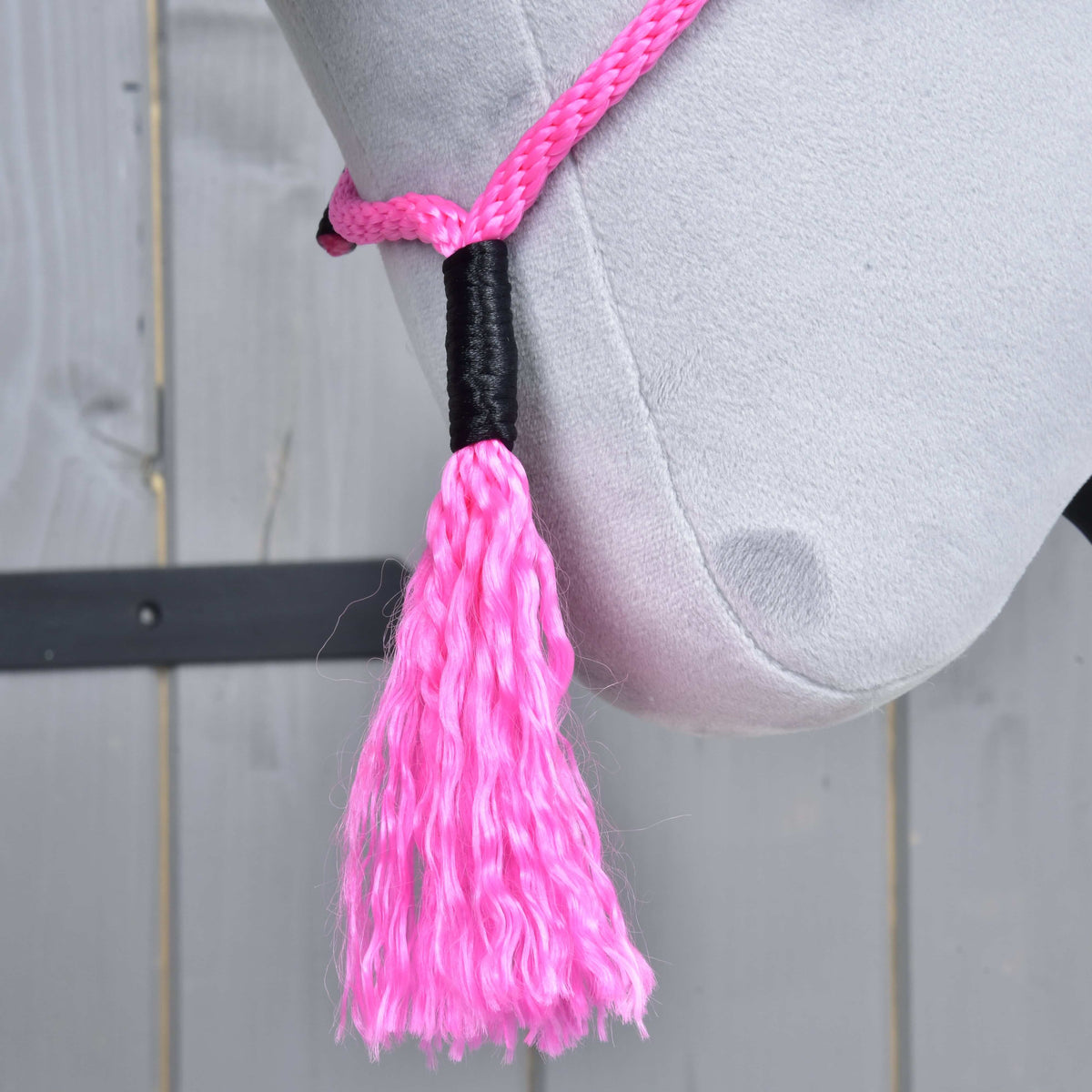 Close-up of the Hobby Horse LarDen "Cordeo Pink Festive"—a light gray plush horse’s head with a pink rope halter and tassel, set against wood. Ideal for hobby horse cordeo or bridleless riding fans.