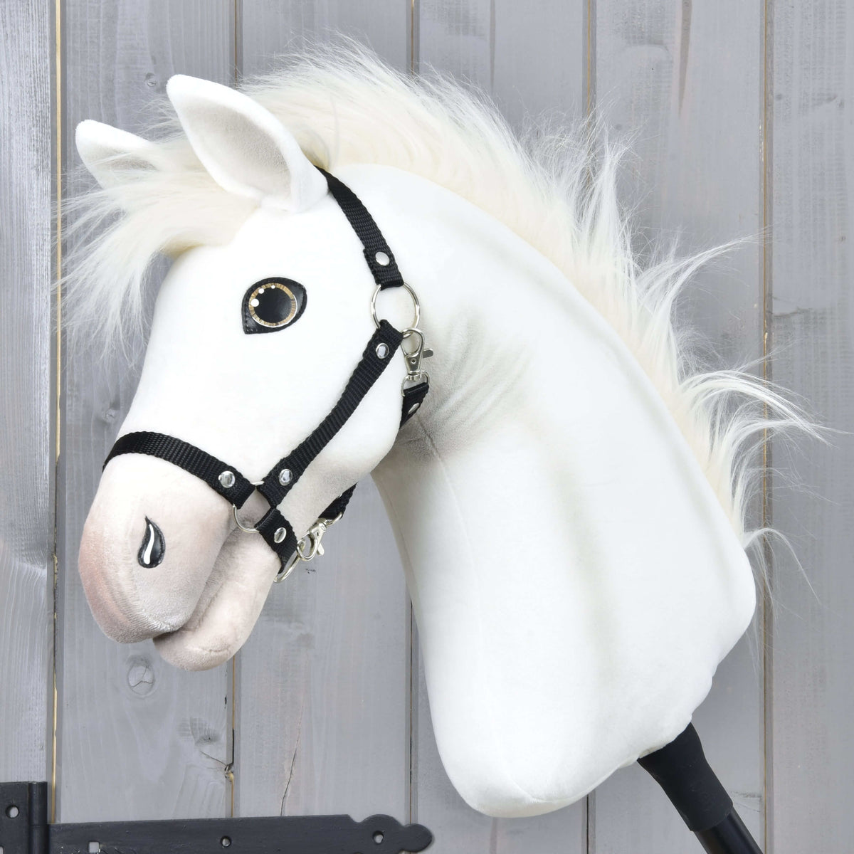 The Hobby Horse Nexus with Black Halter by Hobby Horse LarDen features a white plush Akhal-Teke-inspired head with button eye and fluffy mane, displayed against a wood wall—perfect for any Hobby Horse Nexus enthusiast.