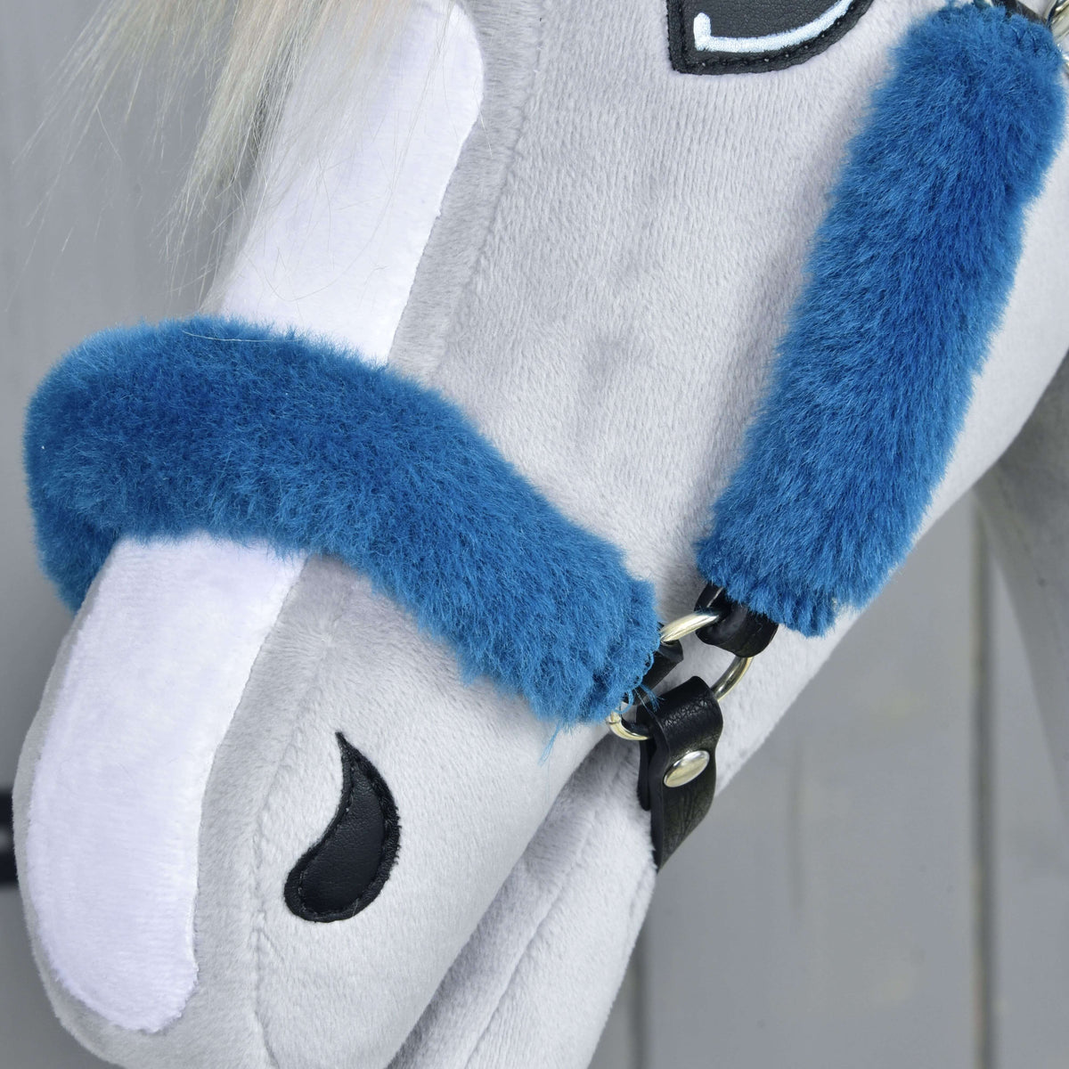 Close-up of a light gray plush toy horse’s head wearing the Fur Halter Teddy Petrol by Hobby Horse LarDen, featuring a blue halter, white mane, and stitched black eye and nostril details against a softly blurred neutral background.