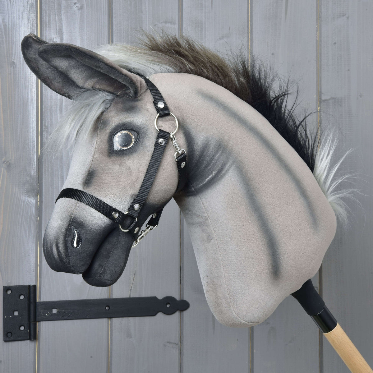 The Hobby Horse LarDen Donkey Olin features a gray plush body, fluffy mane, black halter, and is mounted on a wooden stick, perfect for play or display against any backdrop.