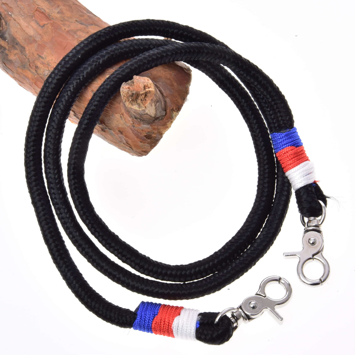 The Hobby Horse LarDen Reins Emblem CZ is a black braided polypropylene rope lanyard with metal clips and red, blue, and white thread accents near the clips, coiled around wood against a white background.