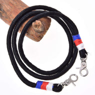 The Hobby Horse LarDen Reins Emblem CZ is a black braided polypropylene rope lanyard with metal clips and red, blue, and white thread accents near the clips, coiled around wood against a white background.