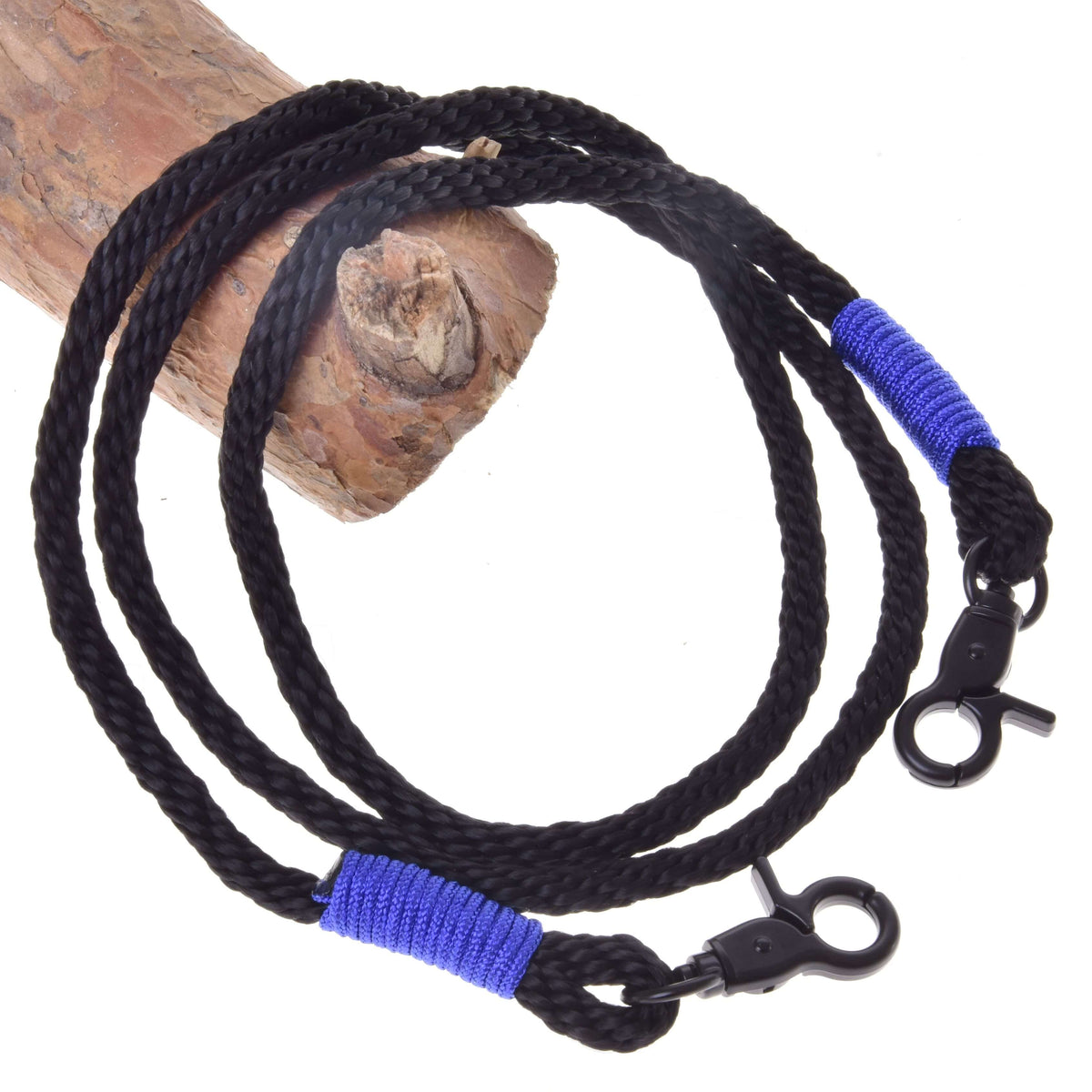 The Reins Basic Blue by Hobby Horse LarDen is a black polypropylene rope with metal clips and blue wraps at the ends, coiled around a wooden log—ideal as handmade or hobby horse reins.