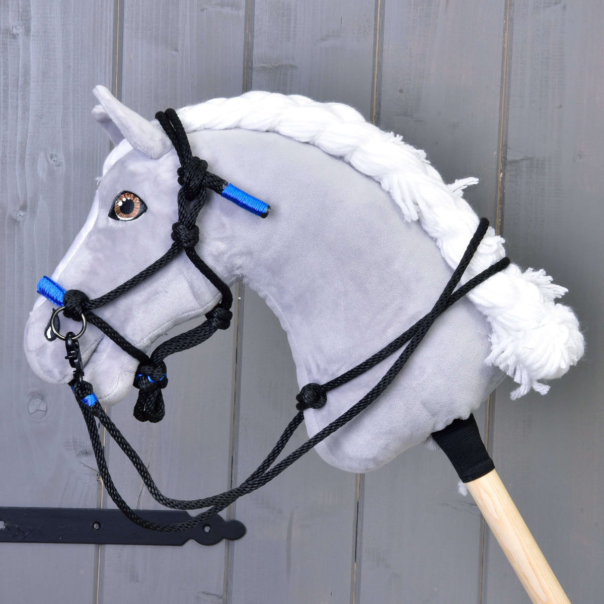 A grey plush Hobby Horse with a white braided mane wears the black and blue rope halter with black rope reins