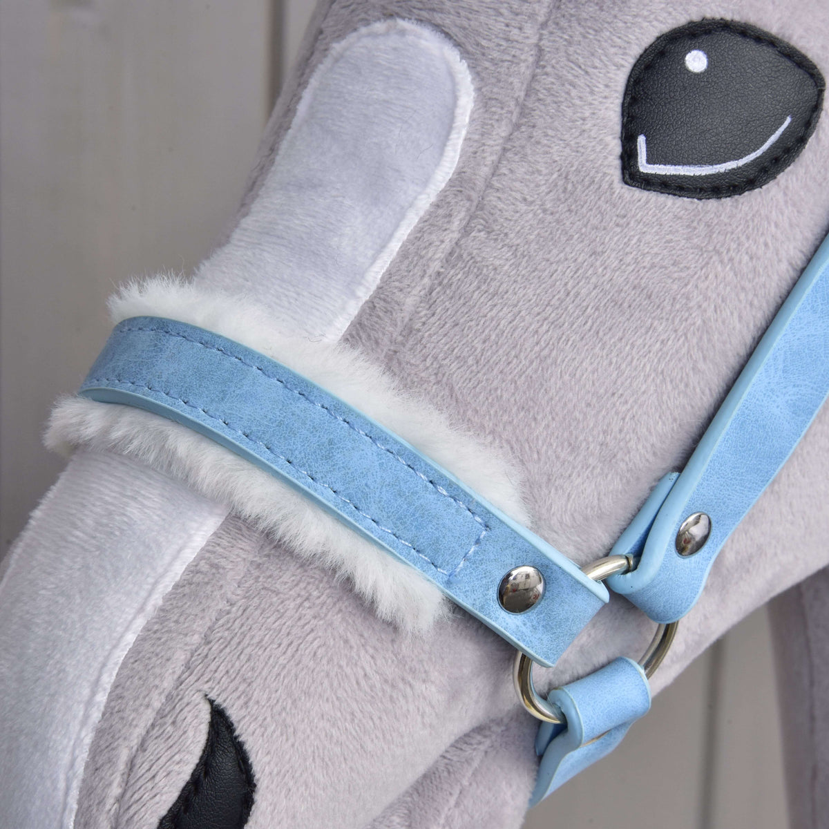 Close-up of a plush toy horse’s head featuring soft gray and white fur, a "Halter with fur - leatherette Pastell Blue" by Hobby Horse LarDen, and embroidered black and white eyes.