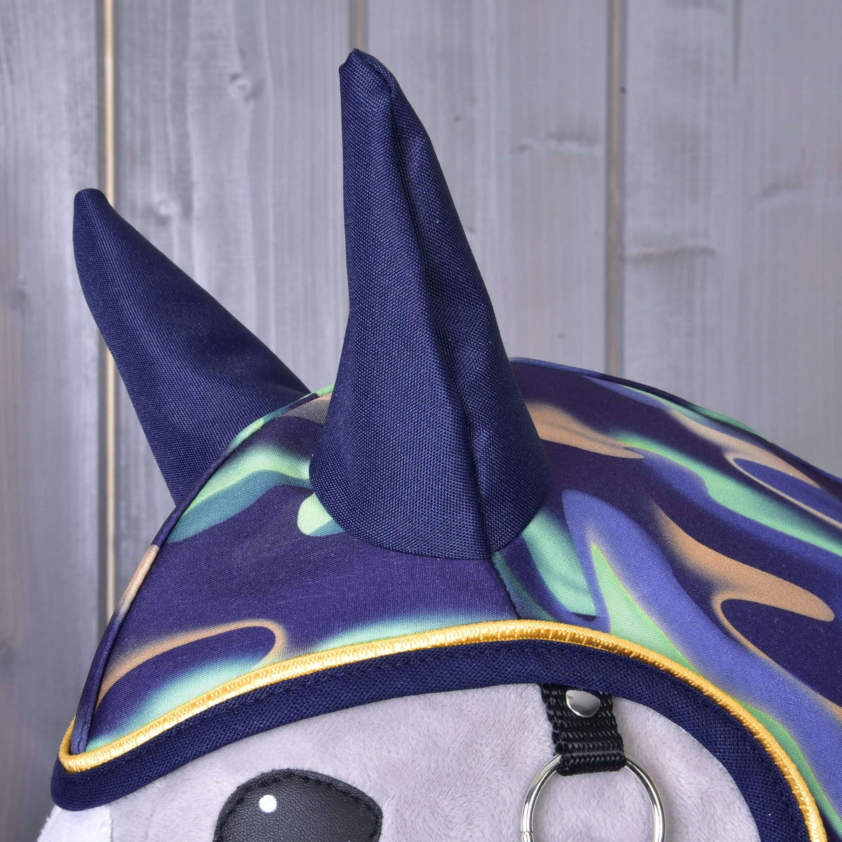 Detalje af de marineblå ører og det bølgede mønster i mintgrøn, lilla og beige med gul kant på regndækkenet Rainbow til Hobby Horse