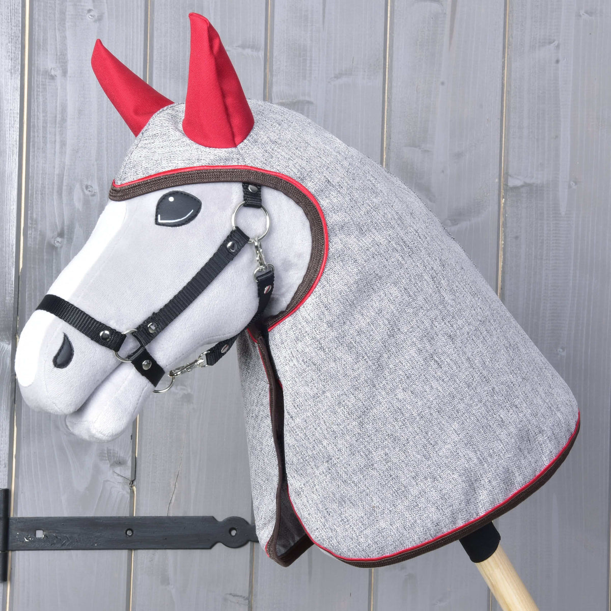 Grey Hobby Horse in a black halter wearing the heathered grey raincoat with red ear covers over its head and neck