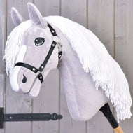The Hobby Horse LarDen Hobby Horse Popcorn with Black Halter features a light gray head, white yarn mane, black halter, and wooden stick handle. Ideal for imaginative play and family horse adventures. Displayed against a wooden wall background.