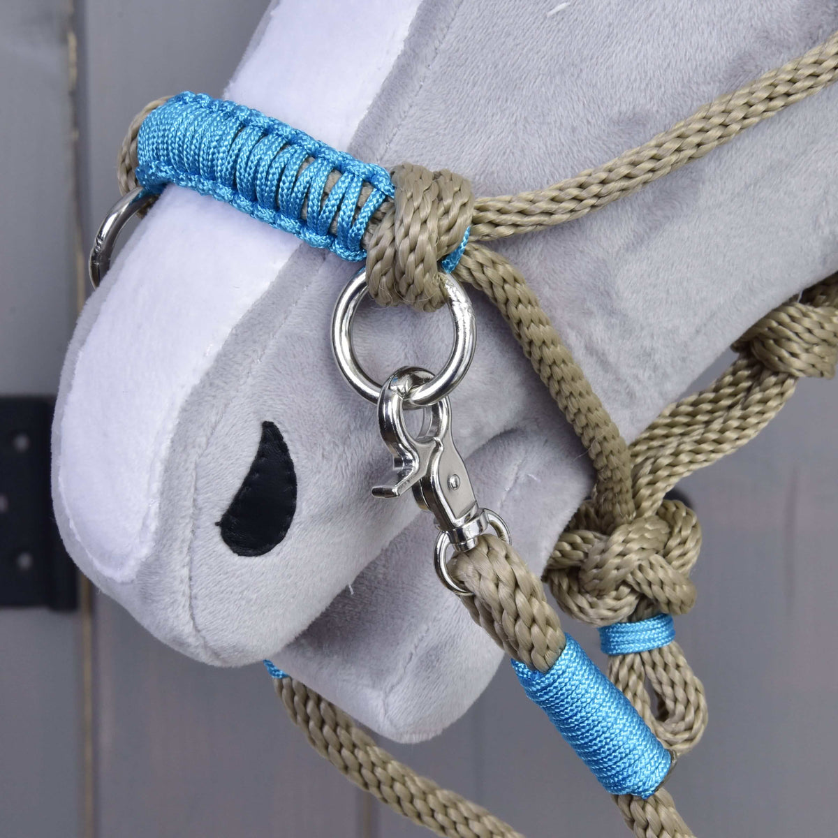 Close-up of a gray Hobby Horse LarDen head wearing the Rope set Nature Blue—a tan and blue halter with metal rings and clip—set against a wooden background.