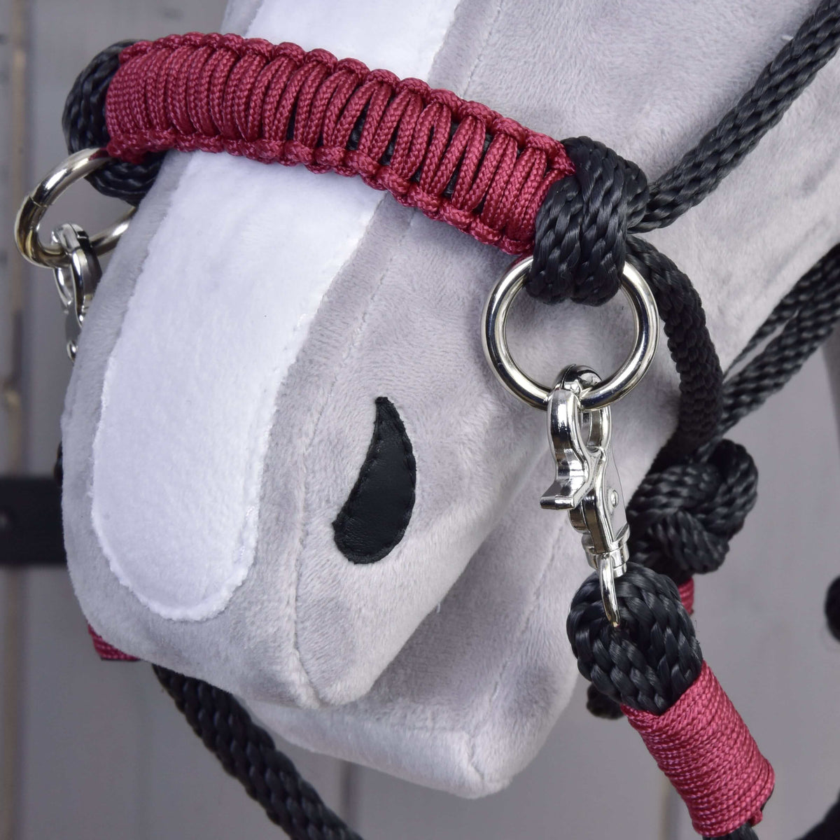 Close-up of a gray and white Hobby Horse LarDen head fitted with a Rope set Maroon, featuring black rope, metal rings, clips, and detailed stitching on the fabric.