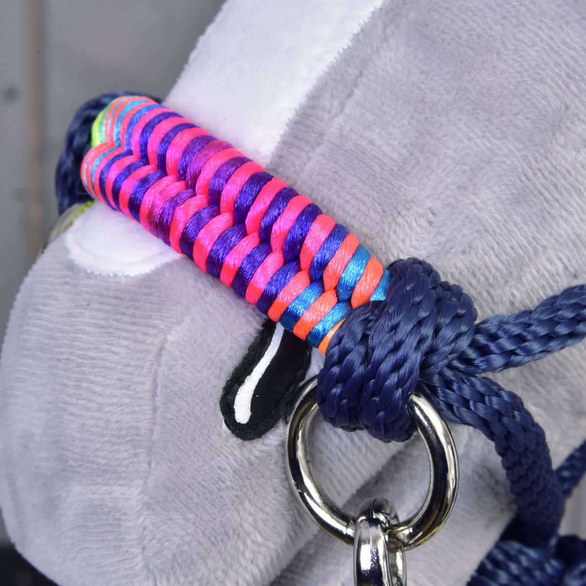 Close-up of a plush animal’s face wearing the Rope set Rosemary by Hobby Horse LarDen: a vibrant, multicolored braided halter with blue rope reins and a shiny metal ring on the side.